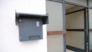 A gray mailbox mounted on a white wall next to a glass door. - Franken Motel (Fuerth)