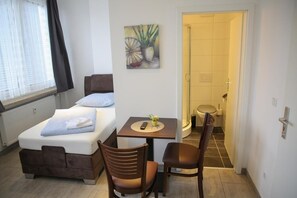 A small, well-lit room with a bed, a table with a remote control, and two chairs. - Franken Motel (Fuerth)