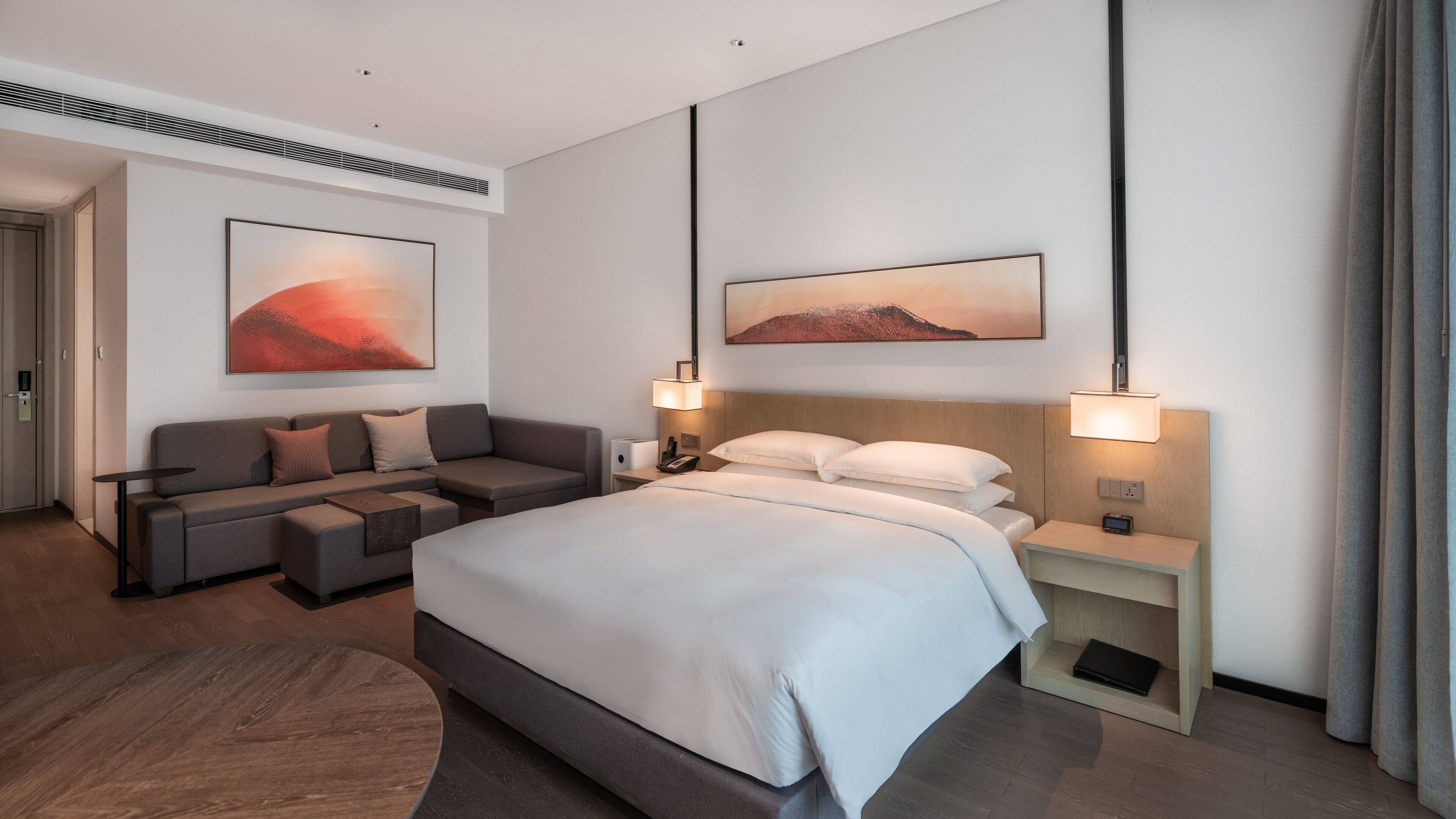 A modern hotel room with a large bed, a sofa, a desk, and two wall-mounted lamps.