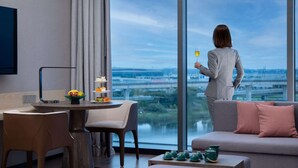 Ein modernes Hotelzimmer mit großem Fenster, einer Essecke mit Tisch und Stühlen, einer Couch und einem Couchtisch.