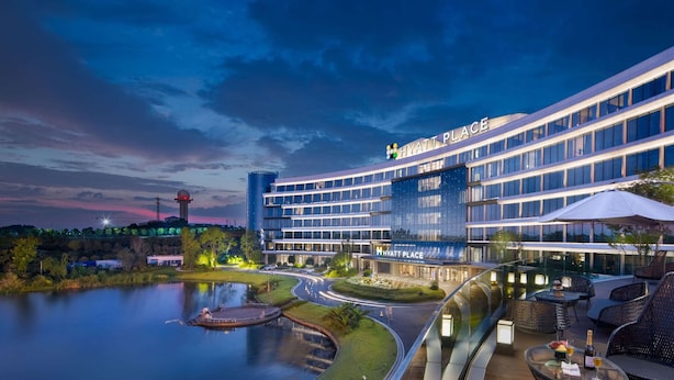 Ein modernes Hotel mit Glasfassade, genannt "Hyatt Place", mit einer angelegten Außenanlage, Sitzgelegenheiten und einem Teich.