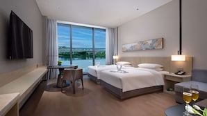 Ein Hotelzimmer mit zwei Betten, einem Schreibtisch, einem Stuhl, einem Fernseher und Seeblick.