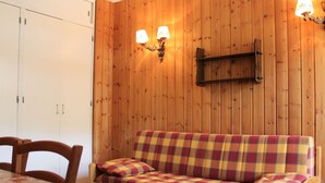 Ein Zimmer mit Holzvertäfelung, einem Karomuster-Sofa, zwei Wandleuchten und einem kleinen Regal.
