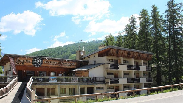 Ein Gebäude mit einem Schild, auf dem 'Le Mouton Noir' und 'Brasserie de Montagne' stehen, was auf ein Restaurant und eine Bar hinweist.