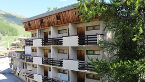 Ein mehrstöckiges Hotel mit Balkonen, einer Holzfassade und einem Bergpanorama im Hintergrund.