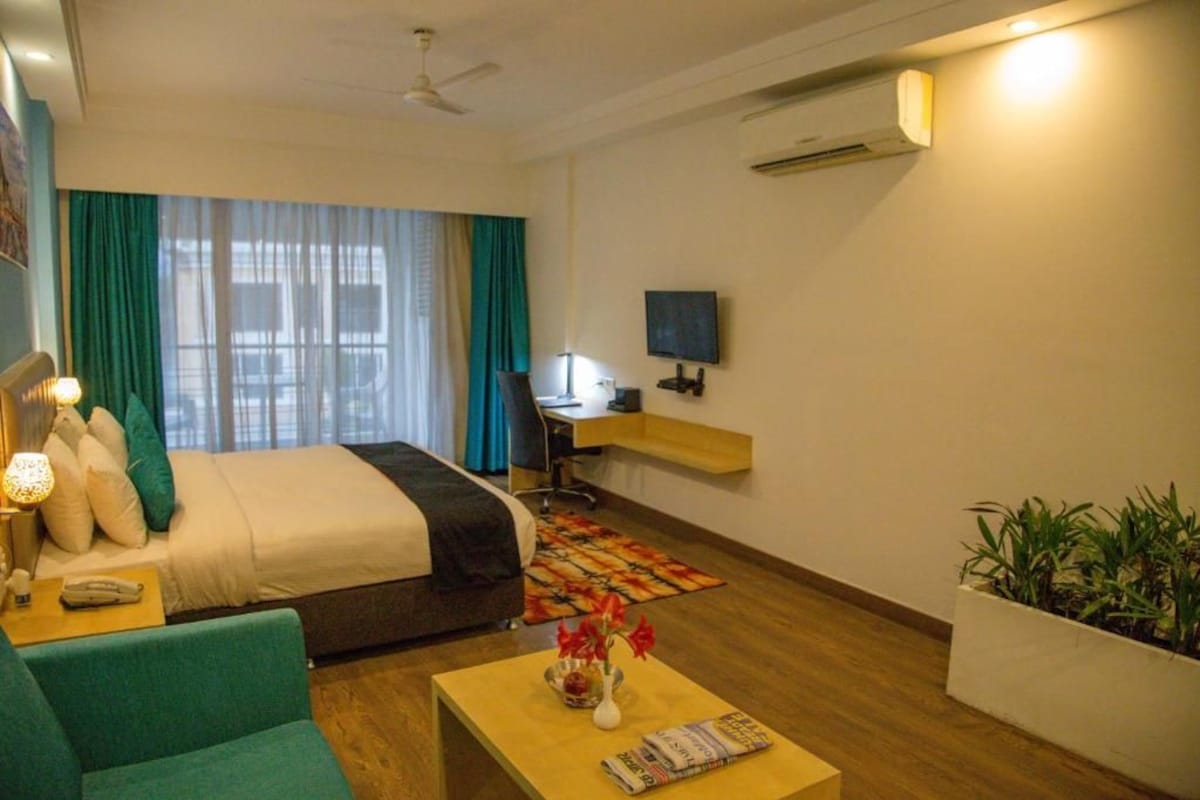 A hotel room with a bed, a desk, a television, a chair, a coffee table, and a potted plant.