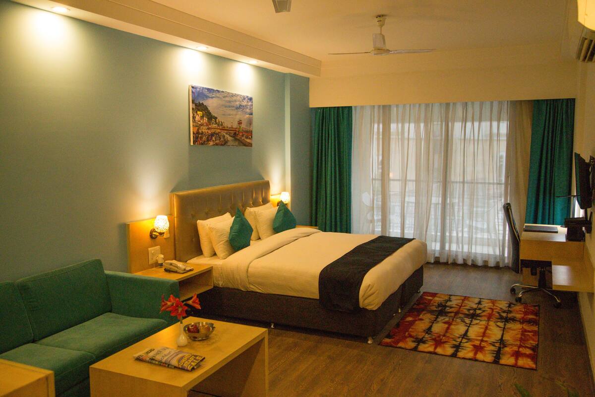 A hotel room with a bed, a sofa, a desk, and a window with curtains.