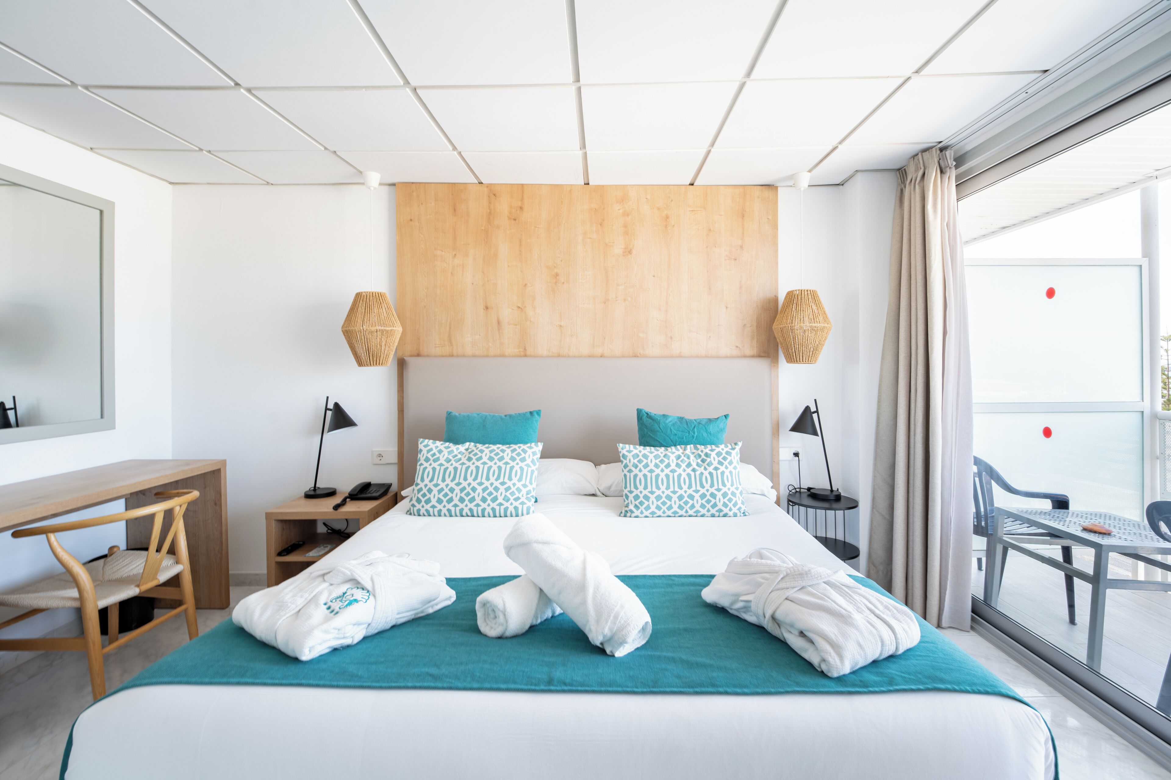 Ein Hotelzimmer mit Bett, Schreibtisch, Stuhl, Nachttisch, Lampe und Blick ins Freie.