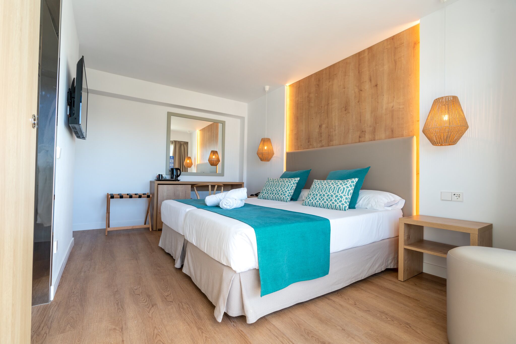 Ein modernes Hotelzimmer mit einem großen Bett, einem Holz-Kopfteil, einem Nachttisch und einem Spiegel.