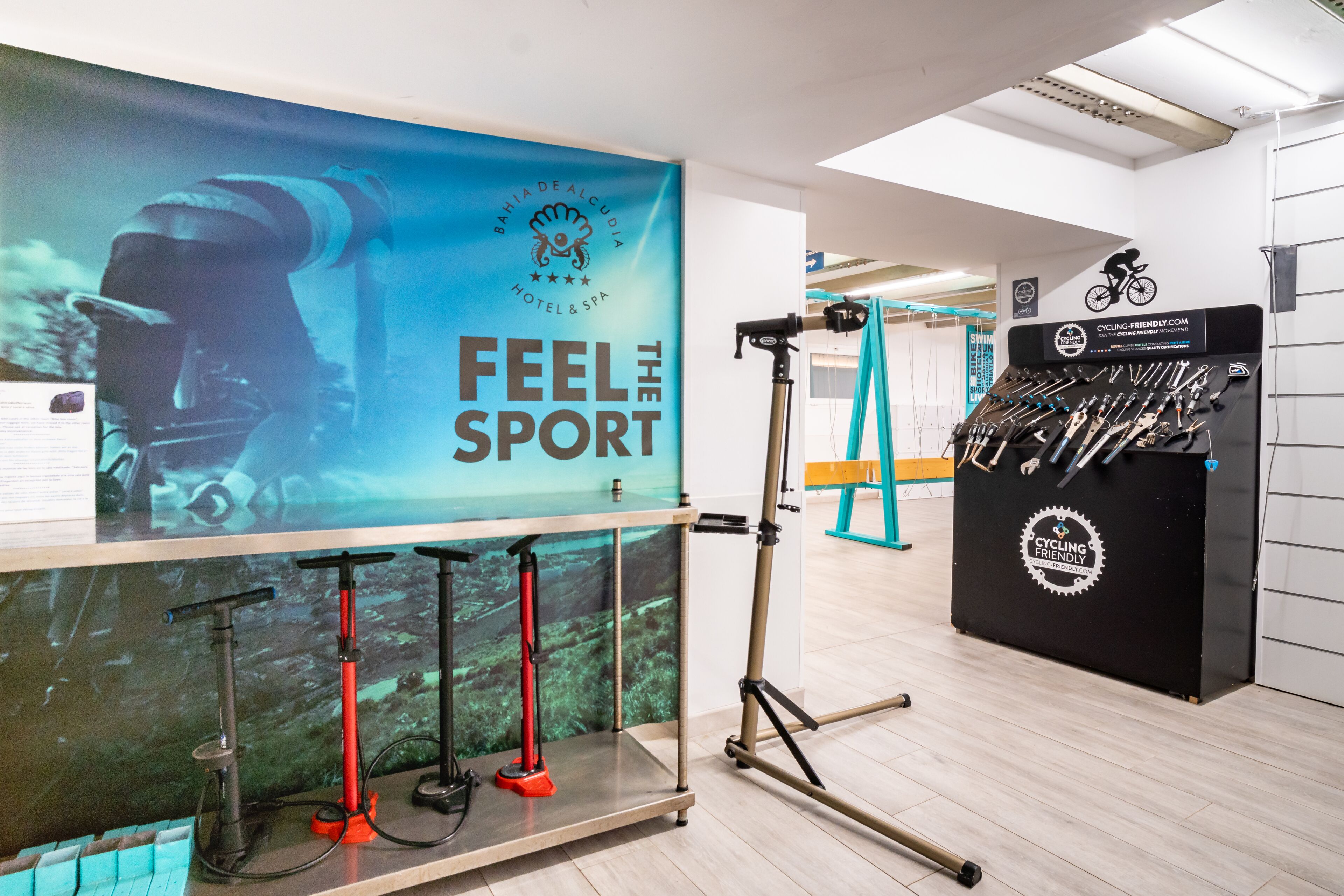 A room with a large banner reading "FEEL THE SPORT", a display of cycling gear, and a wall-mounted camera.