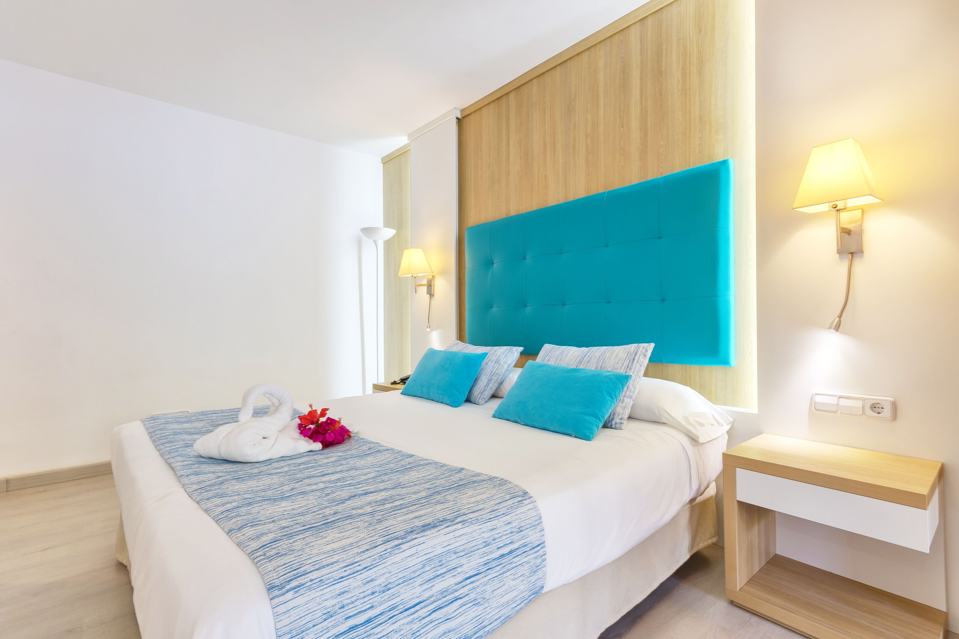 Une chambre d’hôtel moderne avec un grand lit, une tête de lit en bois et deux lampes de chevet.