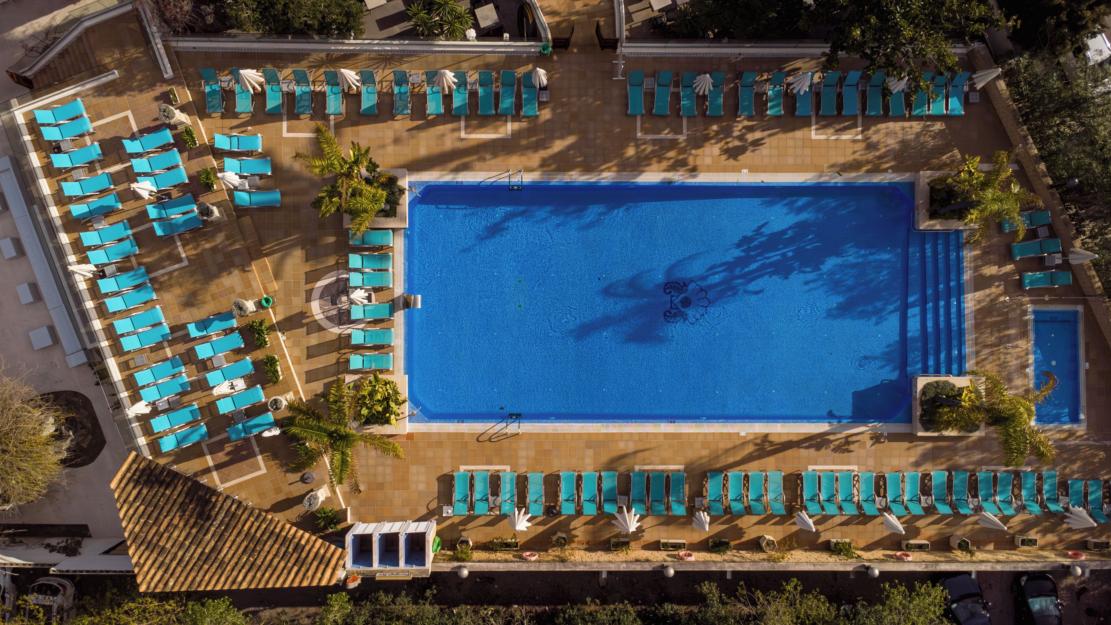 An aerial view of a hotel pool area with multiple lounge chairs and a central swimming pool.