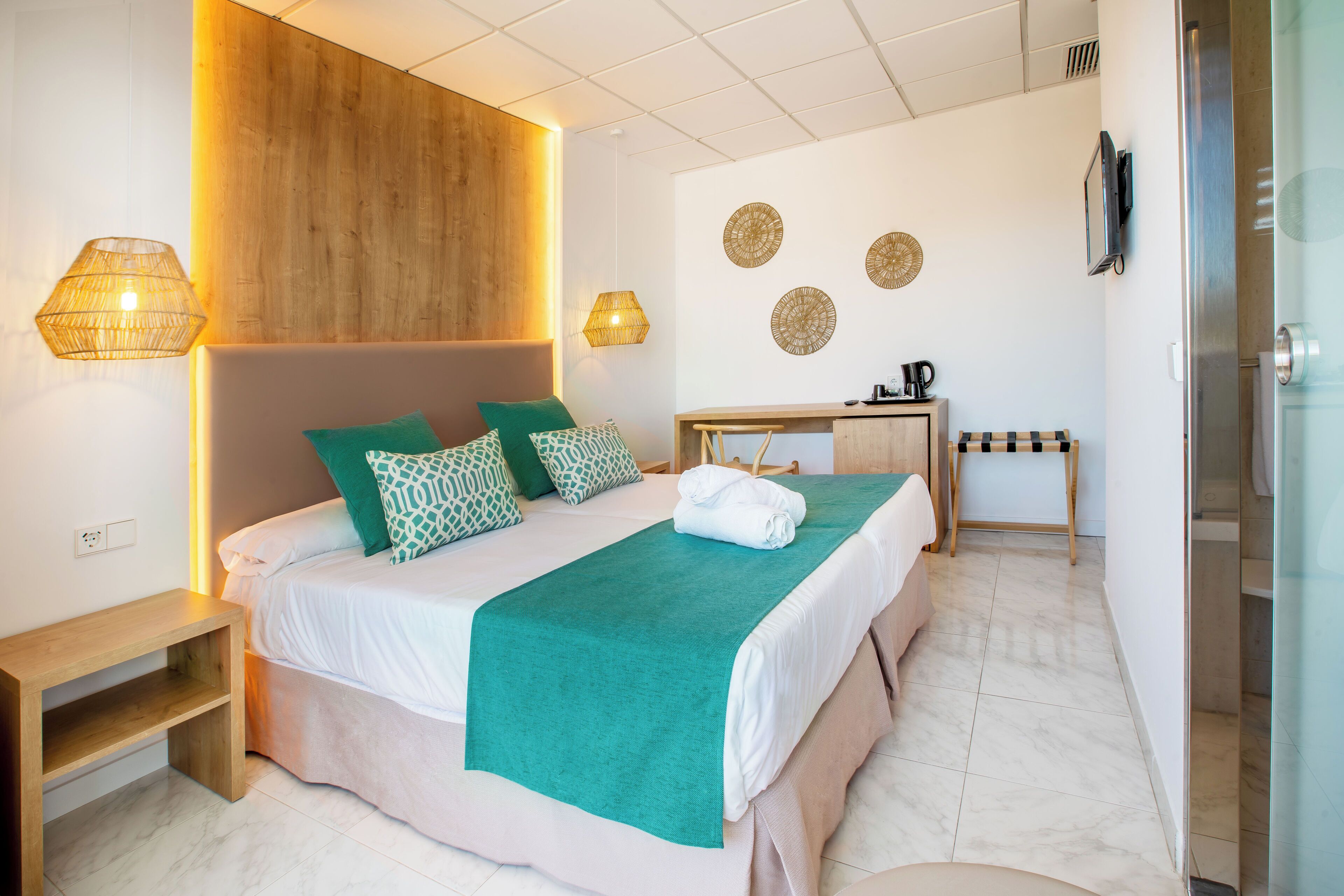 Ett modernt hotellrum med en stor säng, sänglampor, en sänggavel i trä, ett litet skrivbord och en duschhörna.