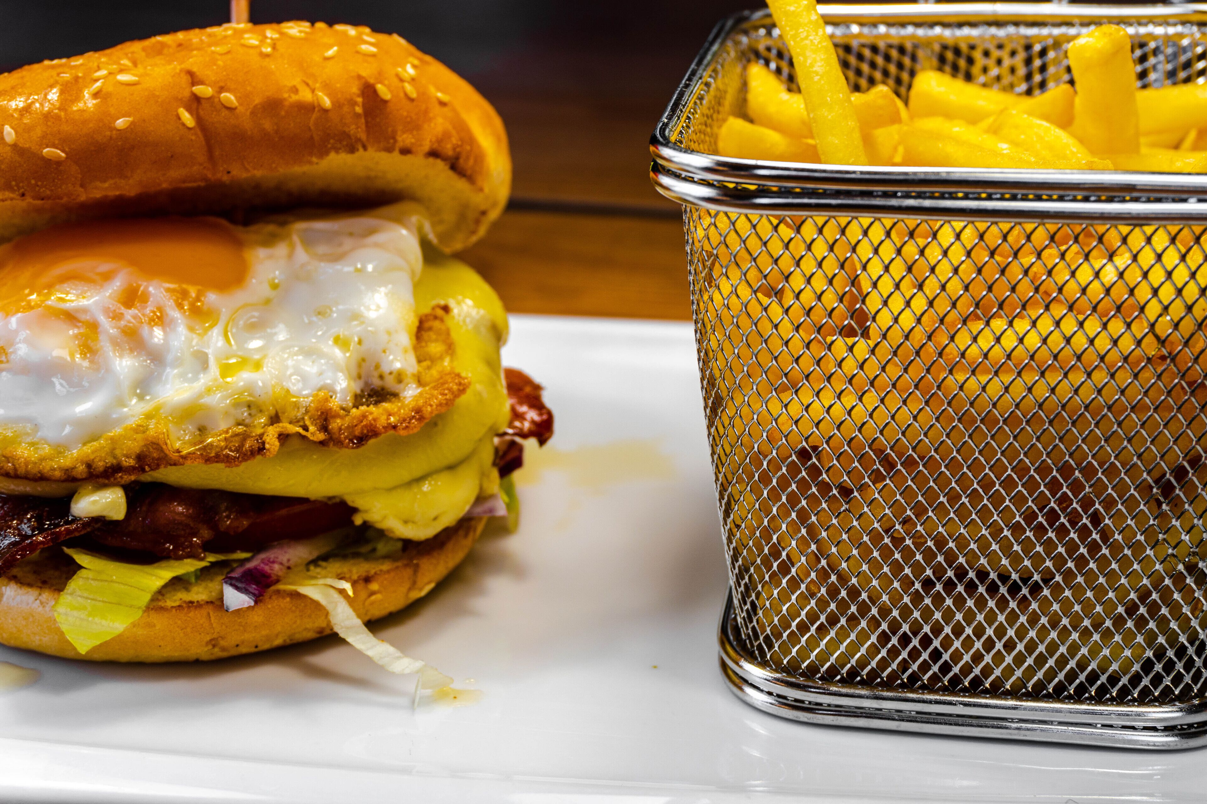 Un sándwich con un huevo frito y papas fritas sobre un plato blanco.