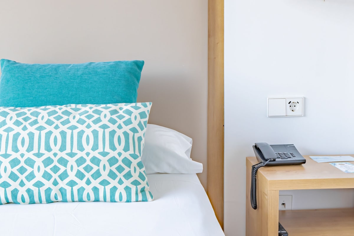 Een hotelkamer met een bed, een nachtkastje met een telefoon en een wandlamp.