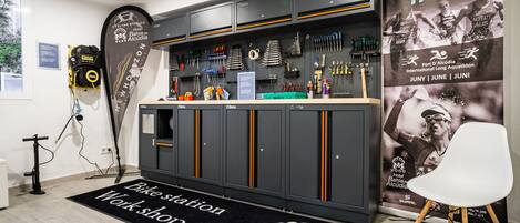 A workshop area with a bike station sign, tools, and a banner for Alcudia Triatlón.