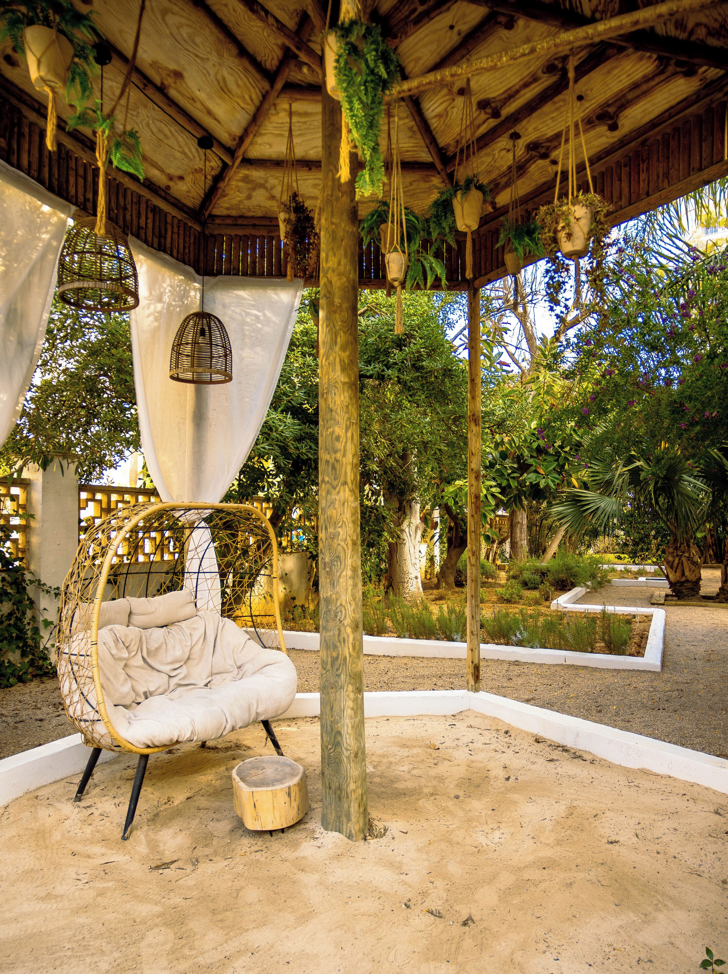A covered outdoor seating area with a hanging chair, a small round table, and hanging planters.