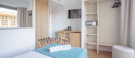 A modern hotel room with a bed, a desk, a wardrobe, and a view of the city.