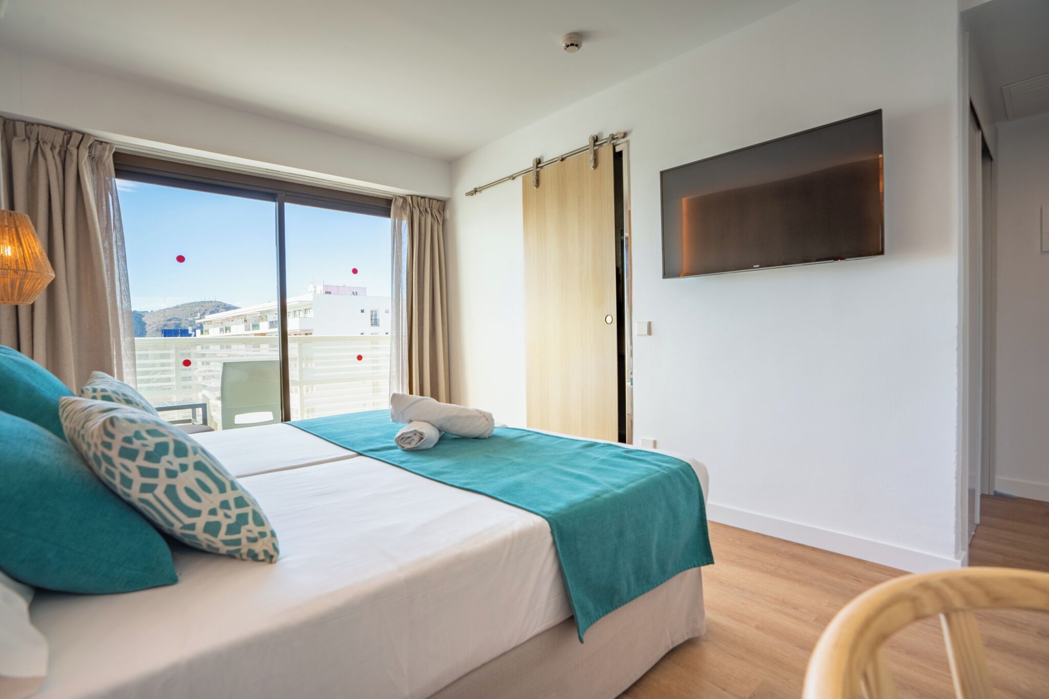 Habitación de hotel con cama, televisión, ventana con cortinas y vistas a edificios.