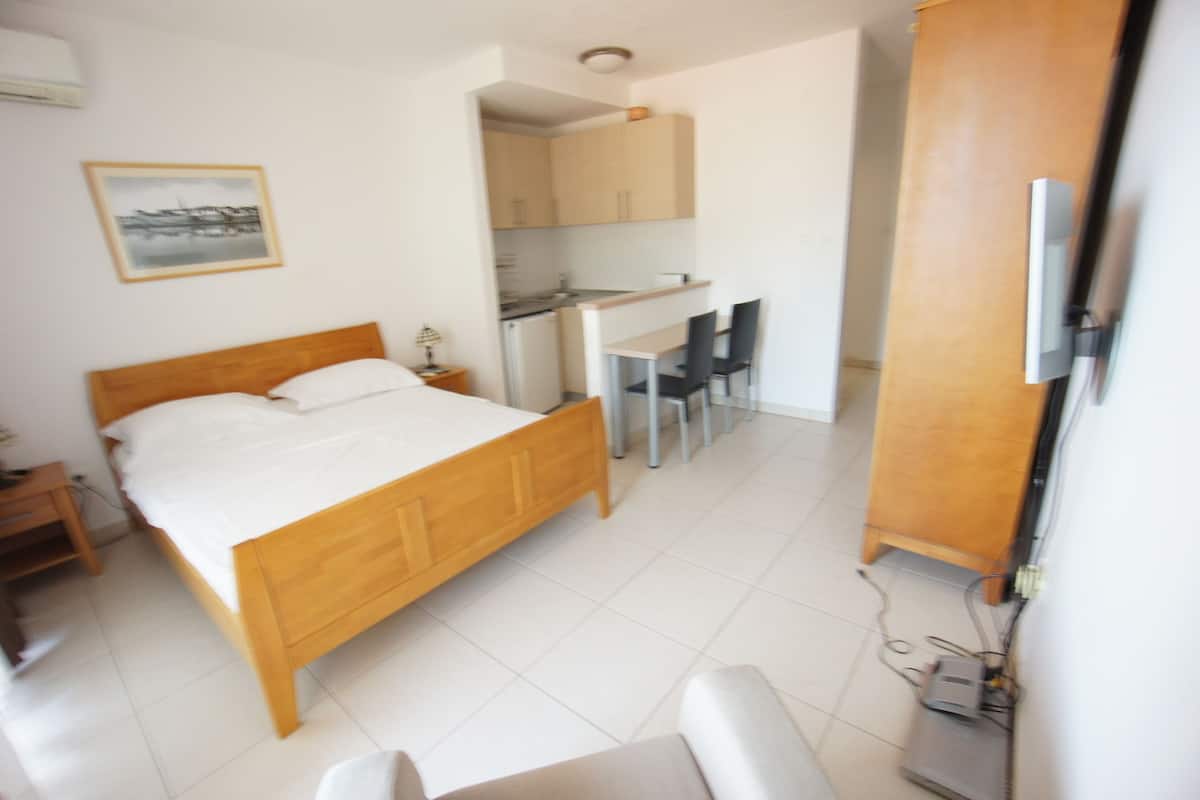 A compact bedroom with a wooden bed, a small desk, and a kitchenette.