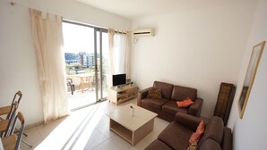 A modern living room with a brown sofa, a coffee table, a TV stand, and a sliding glass door leading to an outdoor area.