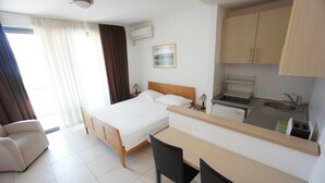 A hotel room with a bed, a desk, a chair, a kitchenette, and a bathroom.