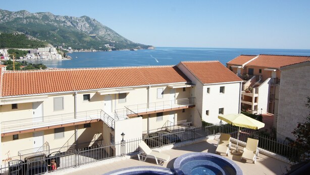 A hotel with a pool, outdoor seating, and a view of the sea and mountains.
