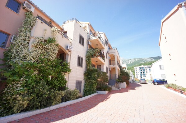A residential street with multi-story buildings, a paved walkway, and parked cars. - Apartments Becici Sunset (Becici)