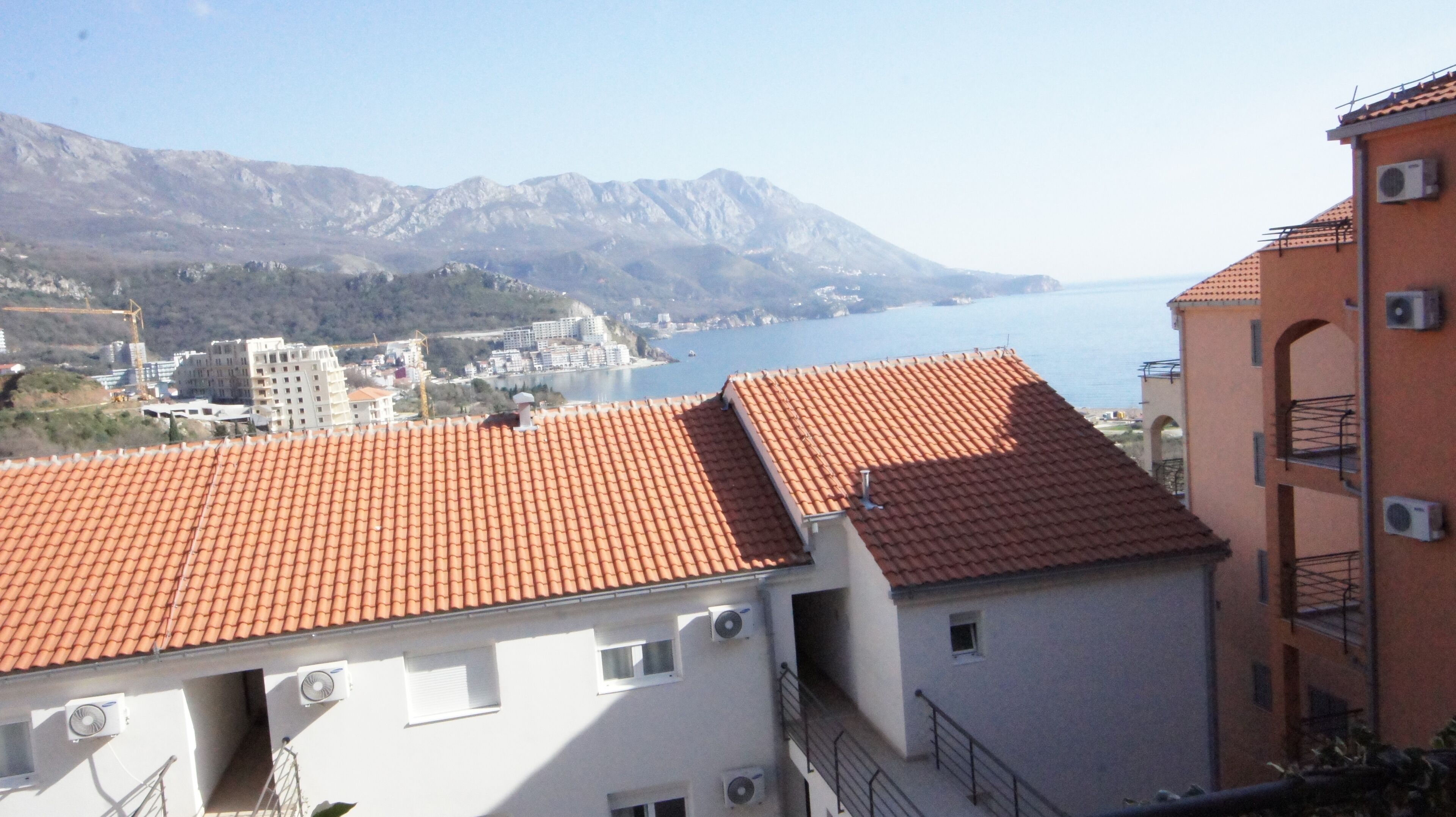 Ένα παραθαλάσσιο κτίριο με κόκκινη κεραμοσκεπή, λευκούς τοίχους και πολλές εξωτερικές μονάδες κλιματισμού.