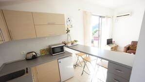 A modern kitchen with a microwave, toaster, and small refrigerator. There is a dining area with a table and chairs. A brown leather chair is visible in the background.