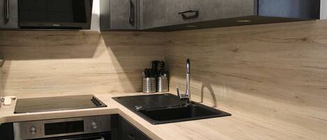 A modern kitchen with a stainless steel microwave, oven, and black sink.