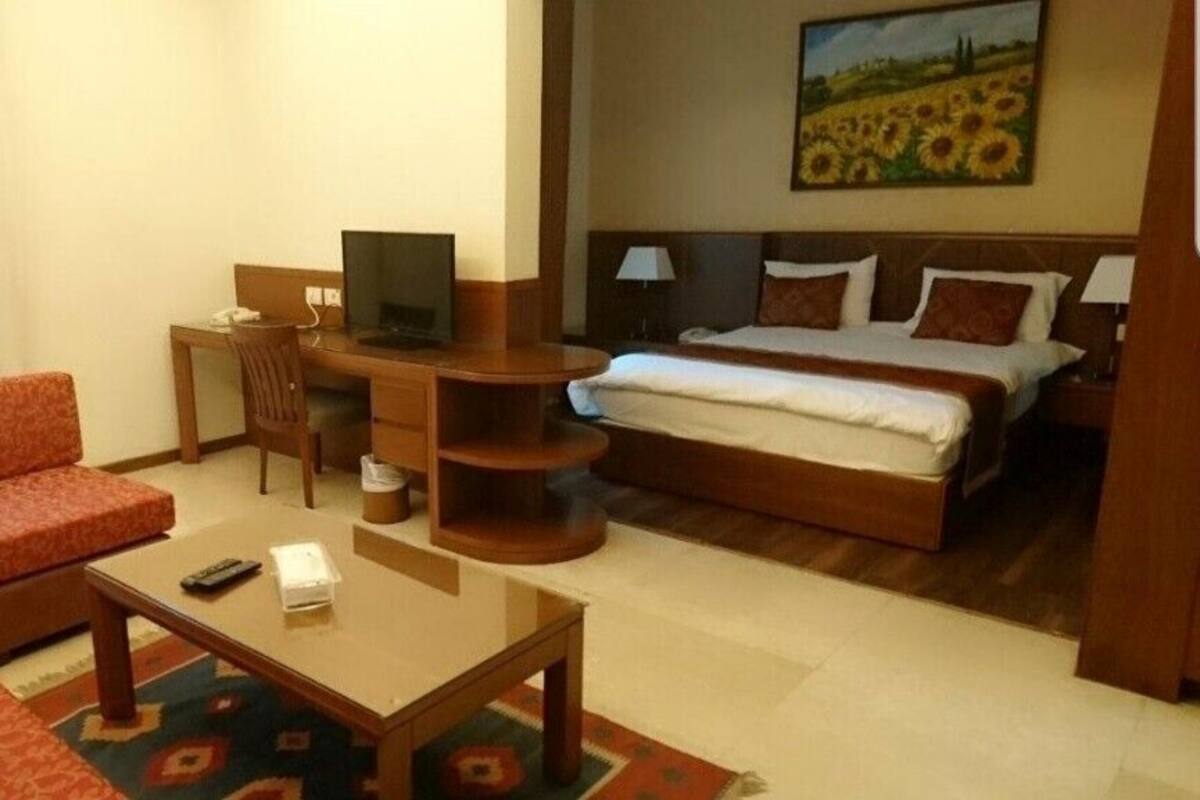 A hotel room with a bed, a desk with a chair, a television, and a sofa.