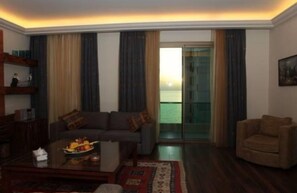 A living room with a sofa, armchair, and a glass door leading to a balcony. - Kings Suite Hotel (Beirut)