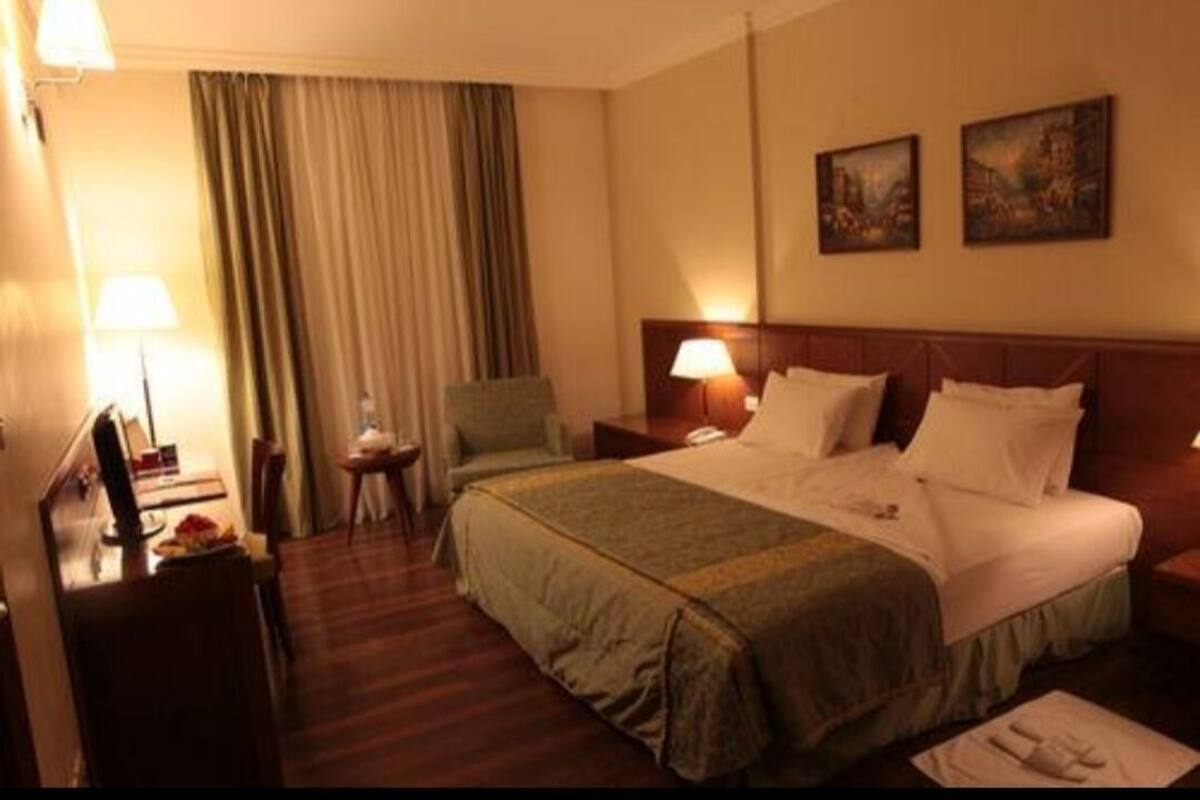 A hotel room with a large bed, a desk with a lamp, a chair, and a dining table.