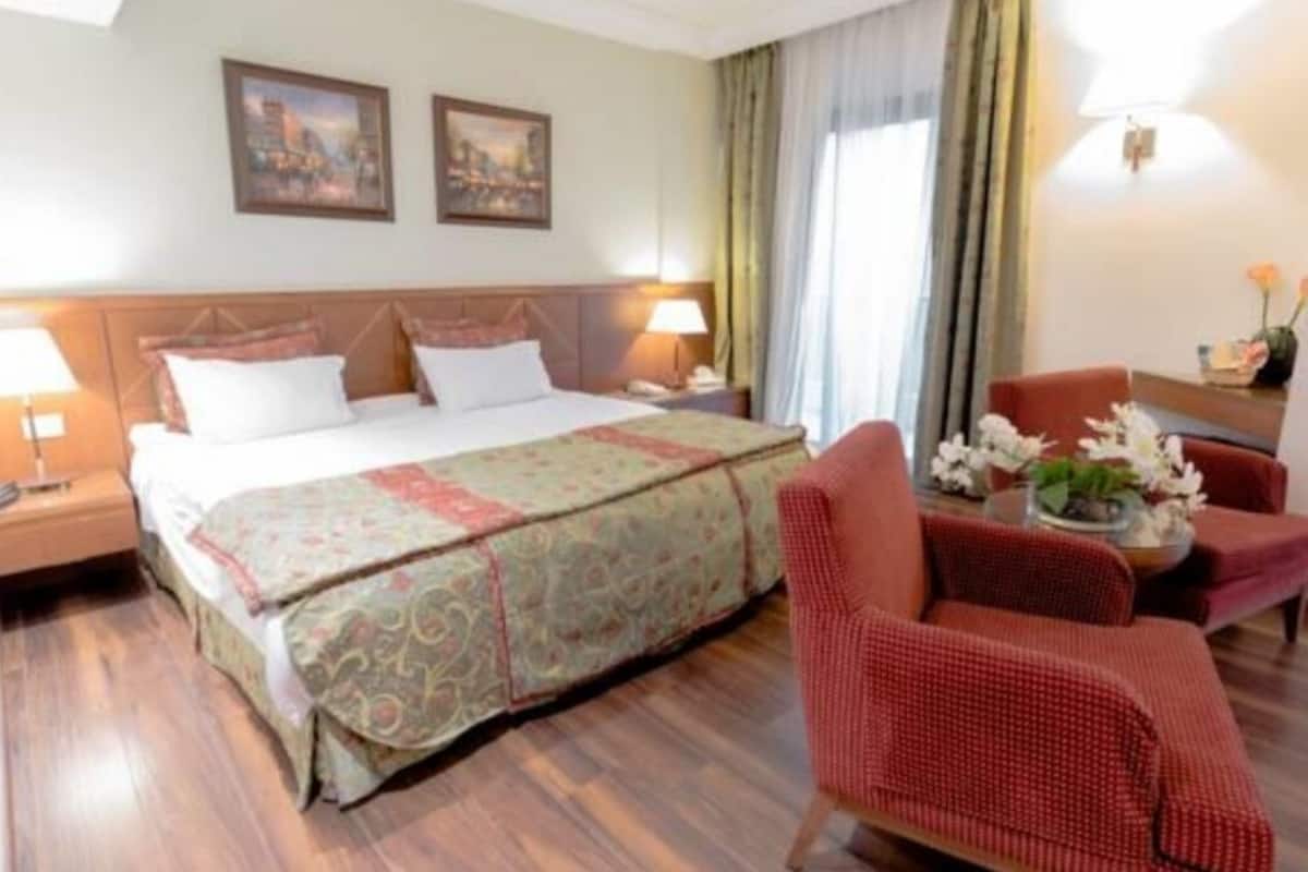 A hotel room with a bed, two bedside lamps, a desk with a lamp, a chair, and a small table with flowers.