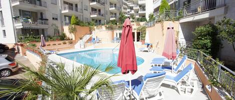 A rooftop pool area with lounge chairs and umbrellas, surrounded by multi-story residential buildings.