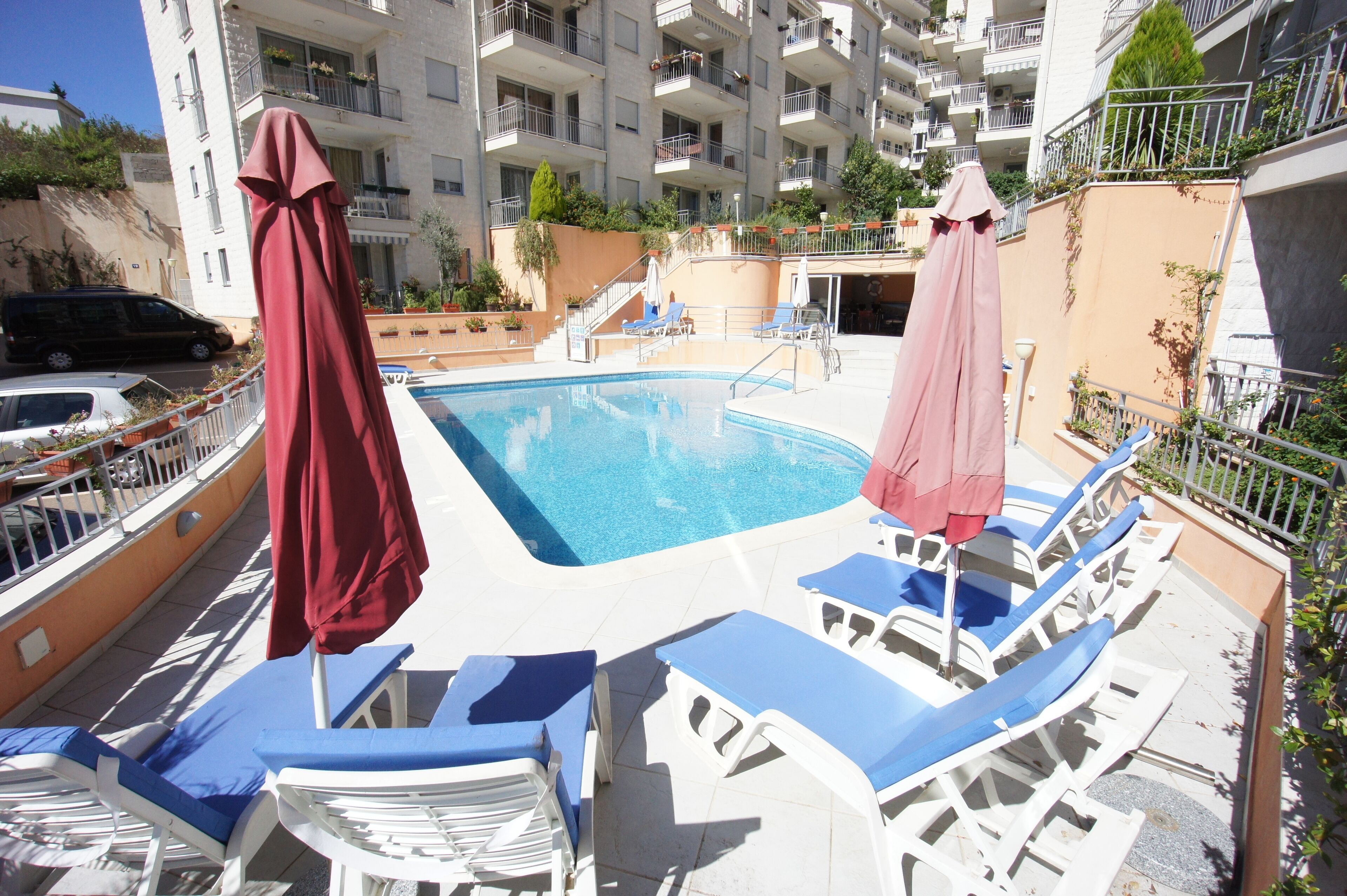 A swimming pool with lounge chairs and umbrellas, surrounded by a multi-story building with balconies.