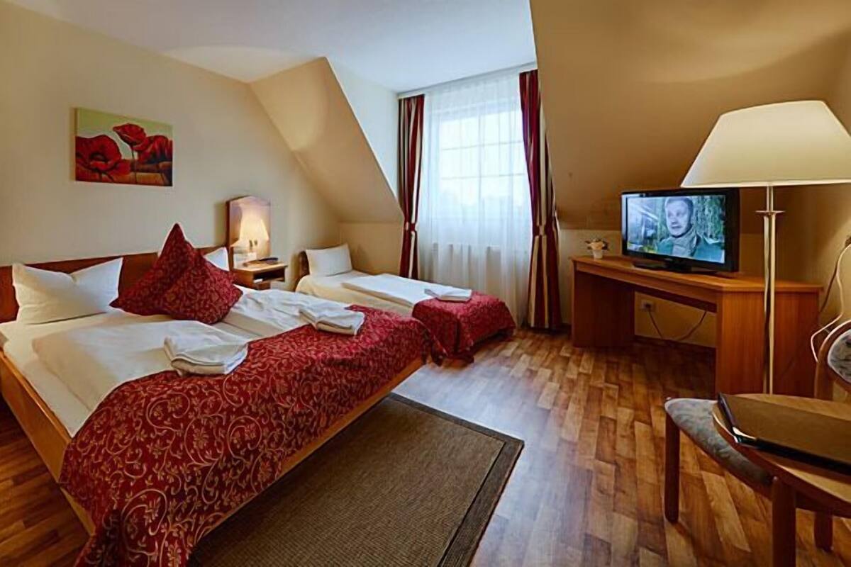 A hotel room with two beds, a desk with a TV, a chair, and a painting on the wall.