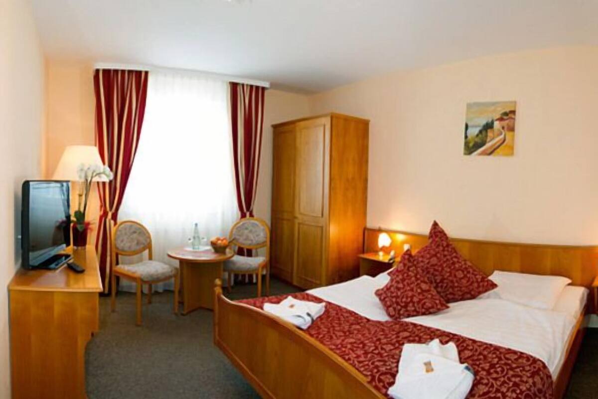 A hotel room with a bed, two chairs, a small table, a TV, and a wardrobe.