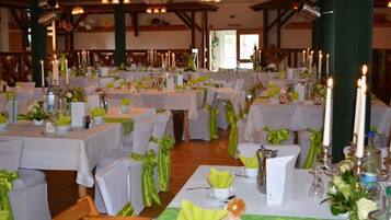 Ein Festsaal mit mehreren runden Tischen, jeder Tisch mit weißer Tischdecke und grünen Bändern dekoriert.