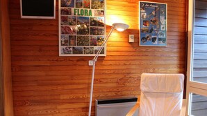 A room with wooden walls, a white chair, a standing lamp, and a poster titled "FLORA" featuring various flowers. - Studio for 4 in the heart of Vars Les Claux (Vars)