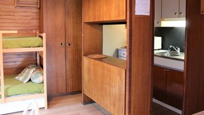 A compact room with wooden walls and a kitchenette. It includes a bunk bed with green bedding, a small table, and a sink. - Studio for 4 in the heart of Vars Les Claux (Vars)
