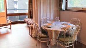A dining area with a round table set for four, surrounded by white chairs with cushioned seats. A wooden bench is positioned against the wall, and a window with curtains is visible. - Studio for 4 in the heart of Vars Les Claux (Vars)