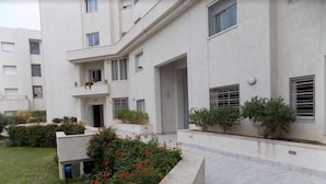 Ein modernes, mehrgeschossiges Wohngebäude mit Balkonen, einer Gartenanlage mit roten Blumen und einem gepflasterten Weg.