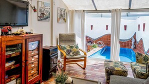 Una sala de estar con televisión, mueble de madera y una silla orientada a una piscina.