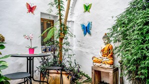 Un patio tranquilo con una estatua de Buda, plantas en macetas y decoraciones de mariposas.