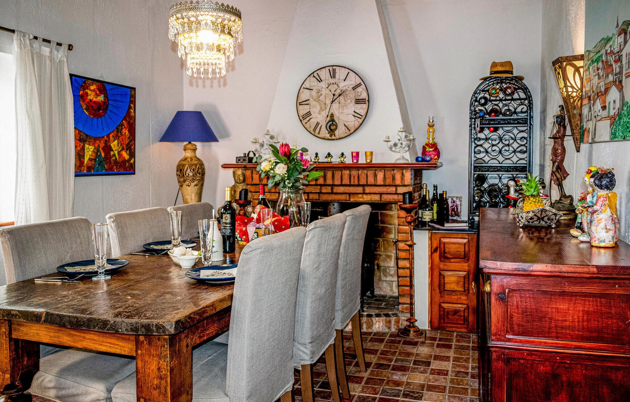 A dining area with a wooden table, chairs, a chandelier, a clock, and a fireplace.