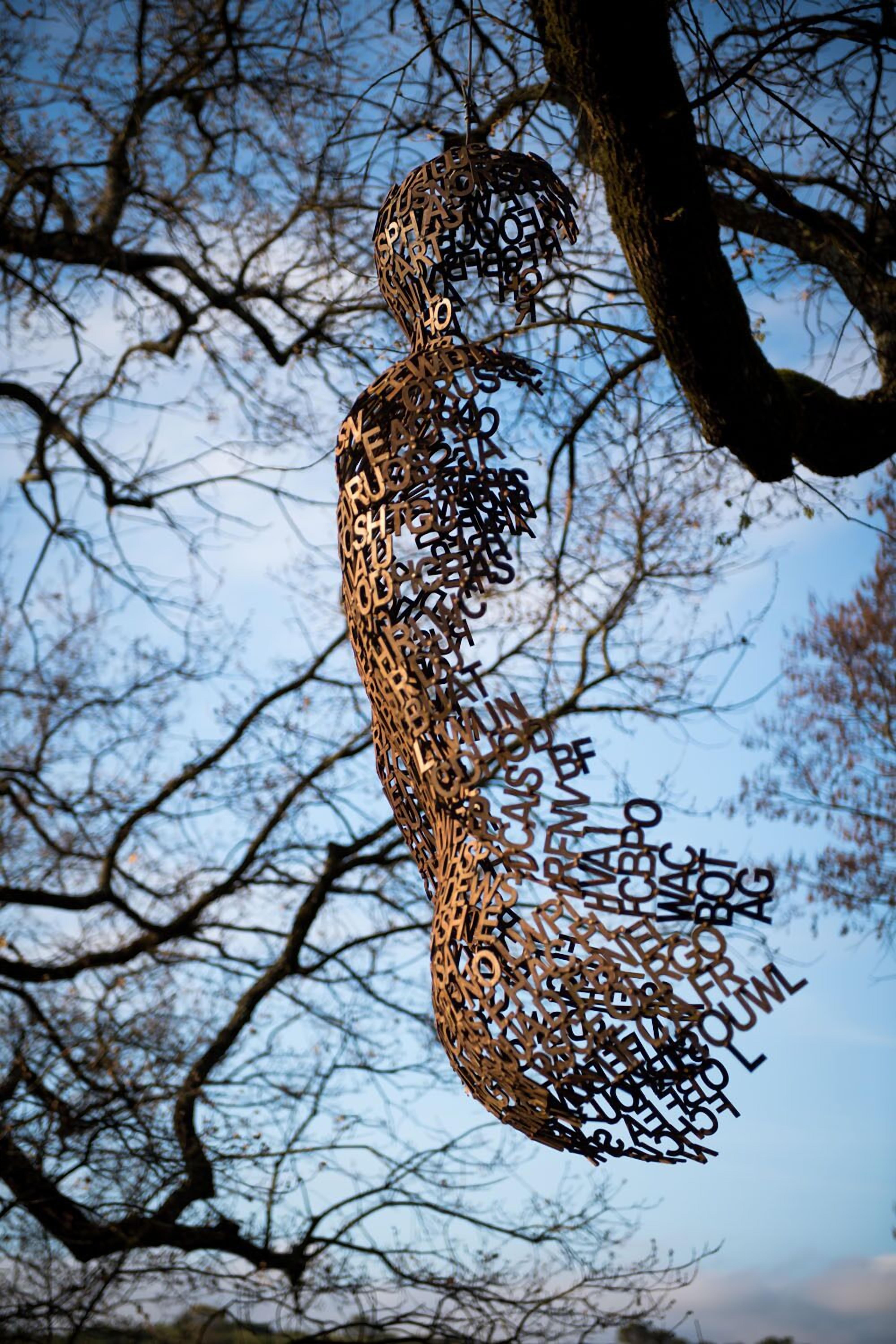 A sculpture of a human figure made from cut metal pieces, set against a backdrop of leafless trees and a clear sky.
