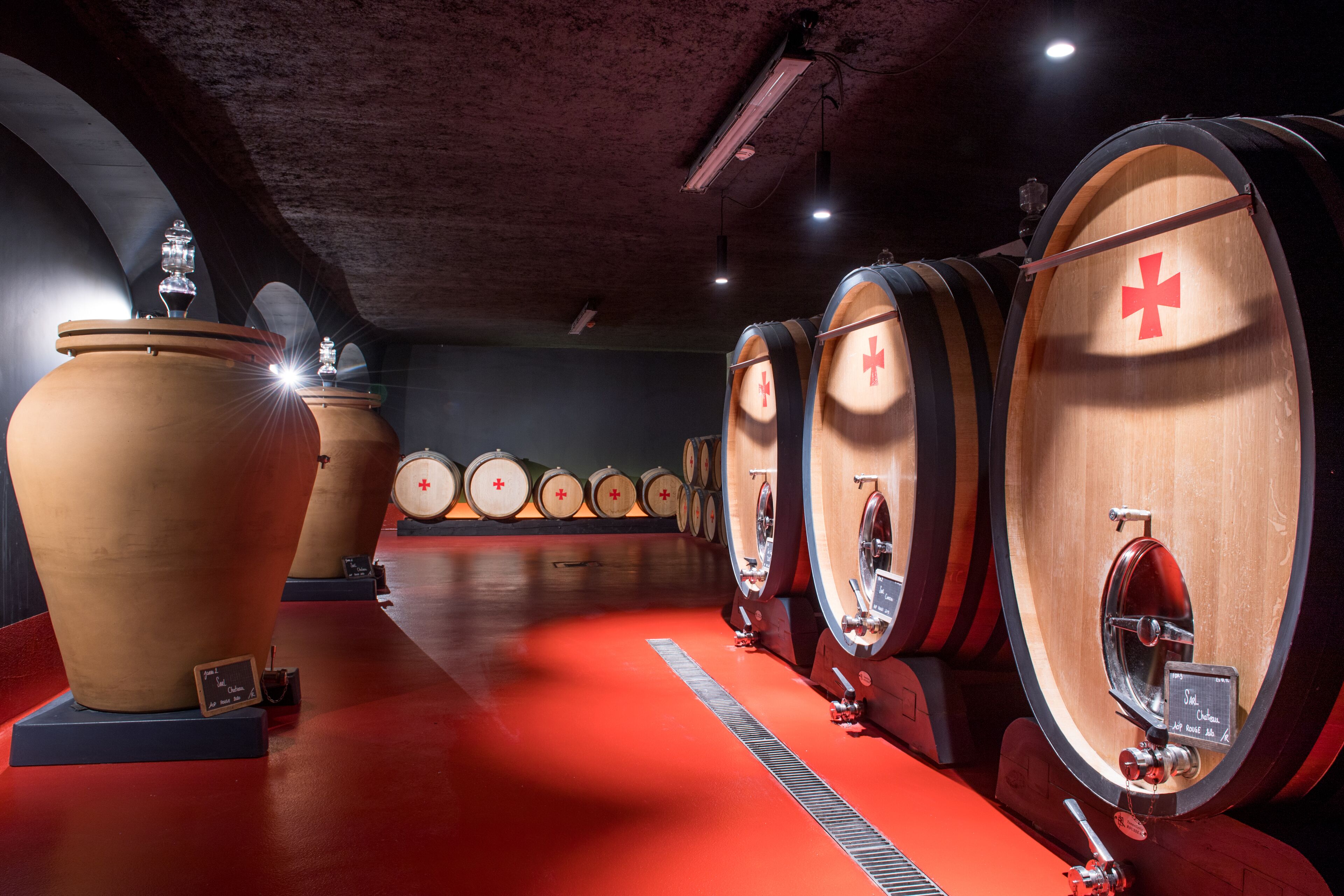 Una bodega con barriles de madera grandes y un piso rojo.