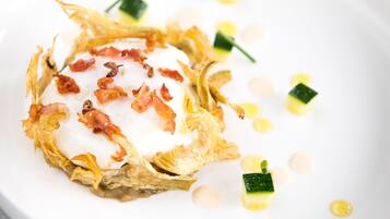A white plate with a dish that includes a crispy base, a creamy topping, and garnishes.